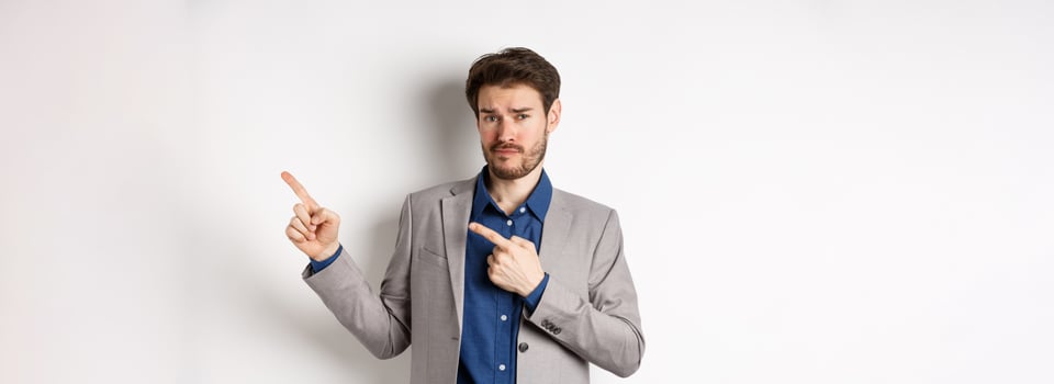Showing bad example. Skeptical businessman look displeased and frowning while pointing at upper right corner banner, standing against white background photo