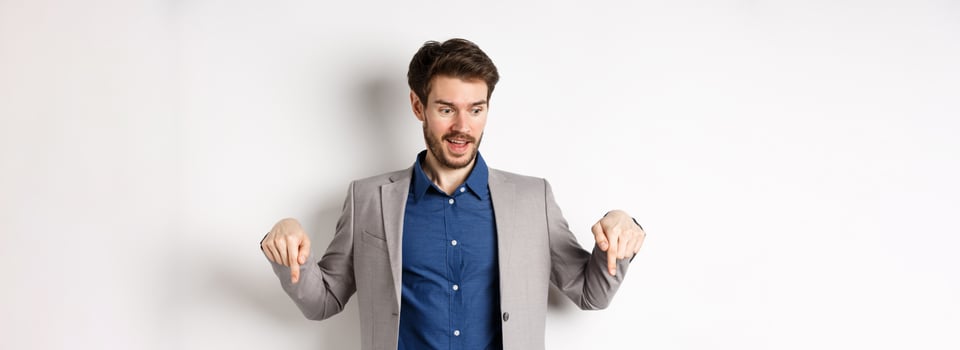 Excited guy in suit smiling and pointing fingers down, looking at special deal with amused face, standing on white background photo