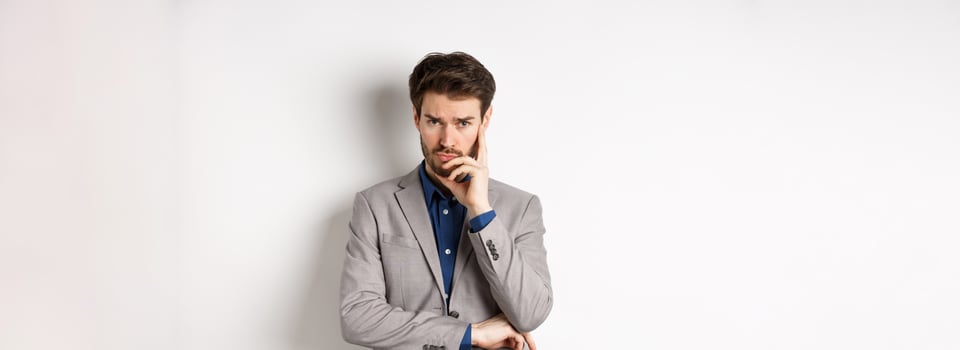 Troubled frowning business man in suit looking at camera pensive, thinking or making decision, standing on white background photo
