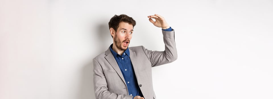 Handsome salesman in suit showing big size, large profit, smiling at camera enthusiastic, standing on white background photo