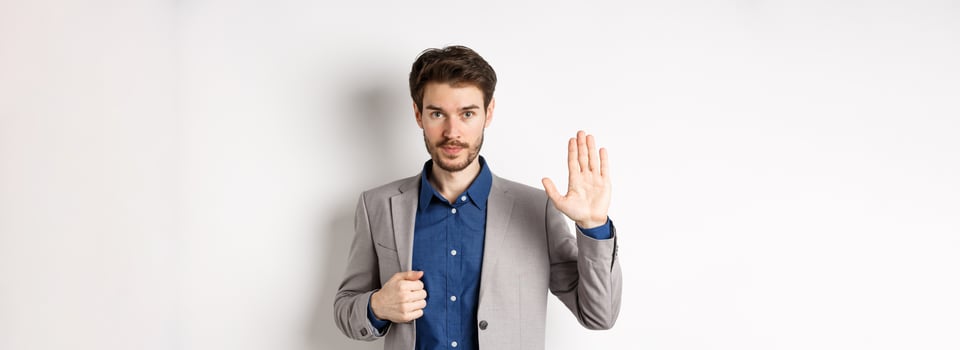 Businessman in formal suit raising hand up to say hello, contactless greeting, smiling friendly, standing on white background photo