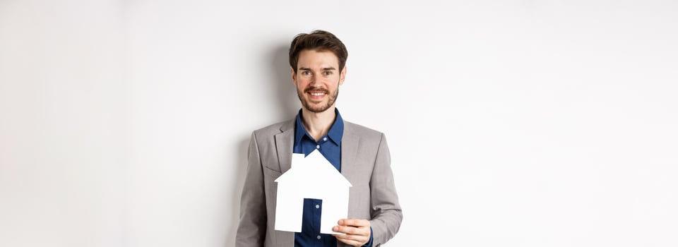 Real estate. Handsome young businessman buying property, holding paper house cutout and smiling, agency advertisement, white background photo