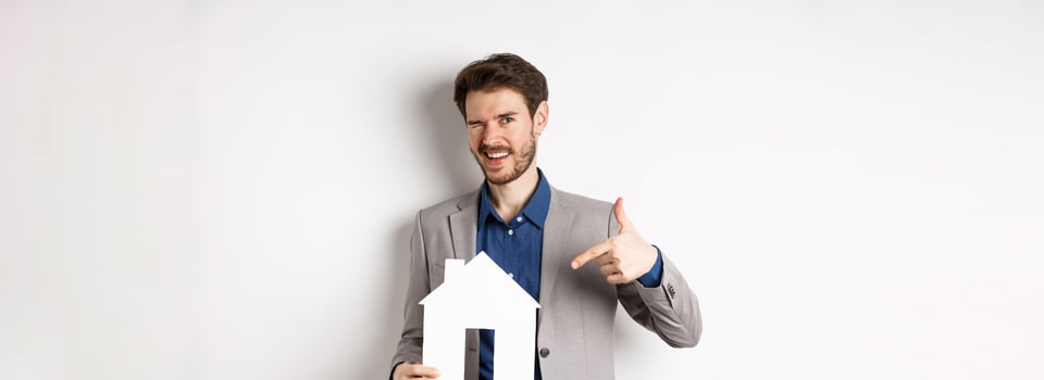 Real estate. Handsome businessman winking and pointing at paper house cutout, advertising company, standing on white background photo