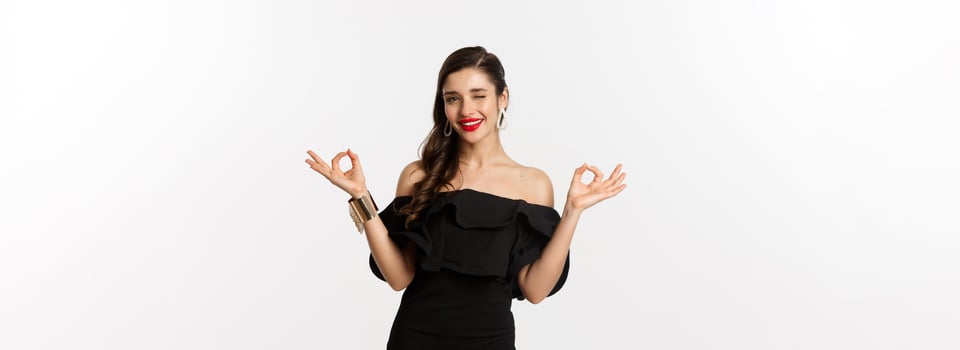 Fashion and beauty. Attractive brunette woman in black dress, showing okay signs and winking at camera, approve and recommend, standing over white background photo