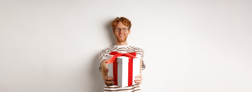 Valentines day and holidays concept. Happy redhead man smiling and giving you gift box, congratulating with birthday, standing over white background photo