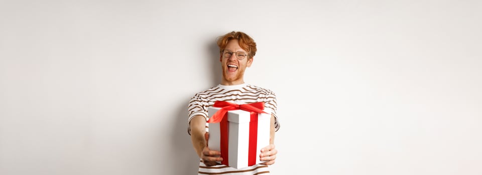 Valentines day and holidays concept. Happy redhead man smiling and giving you gift box, congratulating with birthday, standing over white background photo