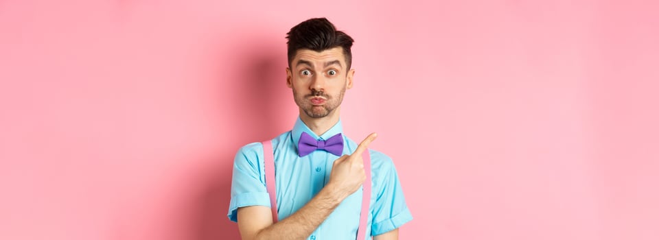 Impressed young man showing awesome promo offer, raising eyebrows and look interested, pointing fingers at upper left corner, pink background photo