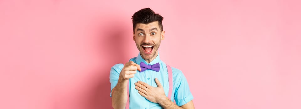 Funny guy laughing at something hilarious, smiling amazed and pointing finger at camera, standing on pink background photo