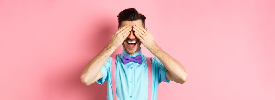 Cheerful young man celebrating, waiting for surprise with closed eyes and happy smile, standing joyful on pink background photo
