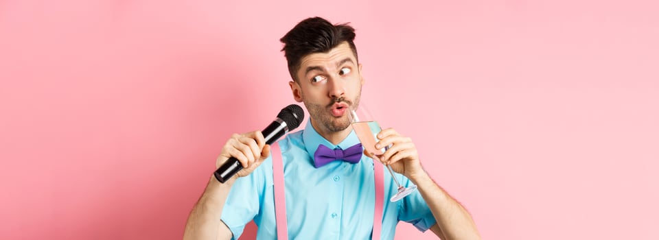 Party and festive events concept. Funny guy singing karaoke, performing song with microphone and drinking champagne from glass, standing on pink background photo