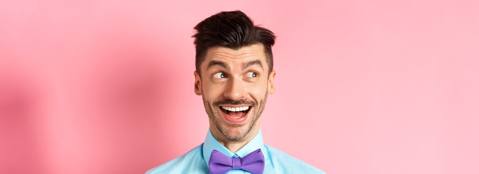 Close up of cheerful smiling guy, looking aside at logo with happy face, checking out cool promo offer, standing against pink background photo