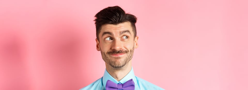 Close-up of handsome smiling guy with moustache, looking left at logo with pleased face, standing on pink background photo