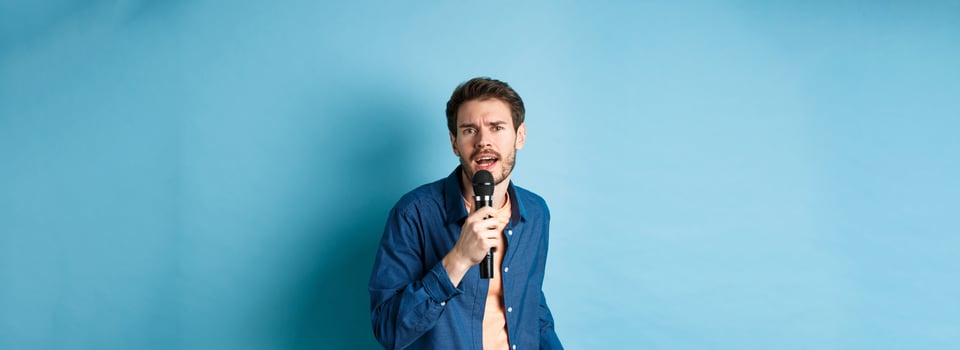 Passionate singer looking at camera, singing in microphone, playing karaoke on blue background photo
