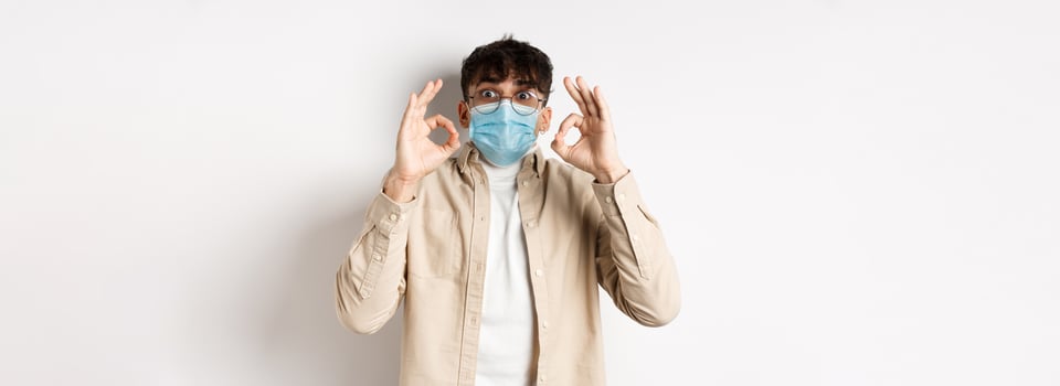 Covid-19, health and real people concept. Excited and impressed guy in sterile face mask showing OK signs in approval, praise cool thing, standing amused on white background photo