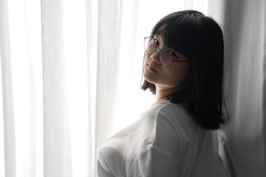 Asian Thai Chinese Woman with her black glasses stands in front of white curtain with the light from outside. It's a cute sexy shot image. photo
