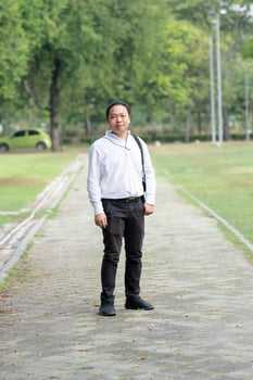 Asian freelance long hair man standing and posting on the walk way in the garden outdoor field with his camera beside him. photo