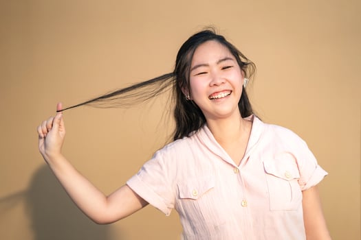 Cute Shy Asian Woman smile and play her hair in orange brown background at outdoor field in sunlight environment. photo