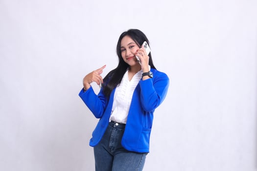beautiful mature office woman wearing blue formal suit standing smiling to camera while using smartphone phone while pointing at it isolated white background. for technology, lifestyle, communication photo