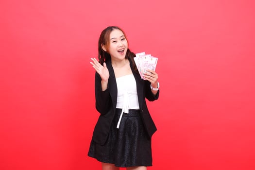 gesture of cheerful young Asian office woman wearing formal black suit holding rupiah currency with palm up, for financial content, business, advertising, transactions photo