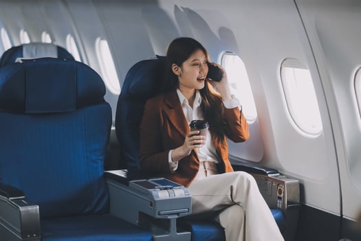 Asian woman looking at phone while sitting on airplane Technology female travelers using mobile smartphones, online apps, and the internet while sitting in airplane seats during travel. photo