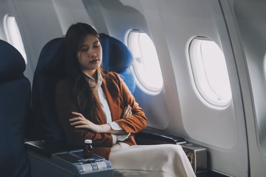 Photo of a frustrated woman sitting on an airplane with her head in her hands. Asian woman sitting in a seat in airplane