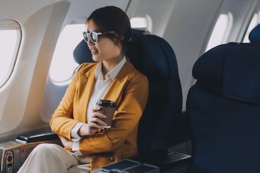 A young Asian woman, seated as an airplane passenger, contemplates dollar bills, reflecting on lucrative opportunities and aspirations towards billionaire status. photo