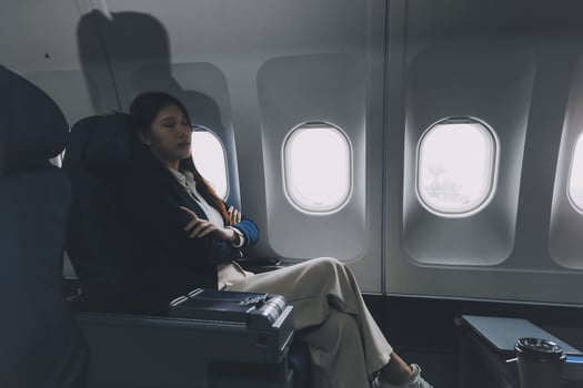 Photo of a frustrated woman sitting on an airplane with her head in her hands. Asian woman sitting in a seat in airplane
