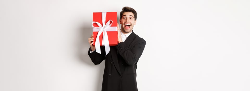 Image of happy good-looking man in black suit, holding box with christmas gift and smiling, standing against white background photo