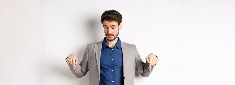 Surprised businessman looking and pointing down with raised eyebrows, see something curious, standing on white background in suit photo