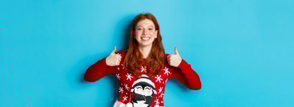 Winter holidays and Christmas Eve concept. Happy smiling girl with red hair, showing thumbs up in approval, praise good product, recommending, standing in xmas sweater photo