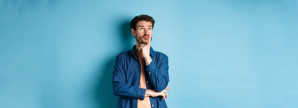 Thoughtful handsome guy making plan, looking up pensive, imaging things, standing on blue background photo