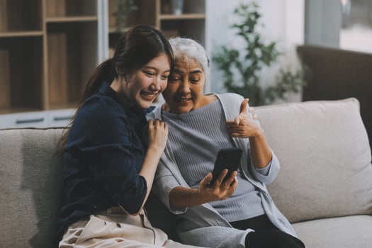 Cheerful mother and pretty teenager kid relaxing at cozy home, using mobile phone for Internet communication, resting on sofa with digital gadget, enjoying leisure, looking at camera photo