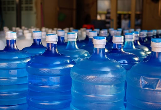 Many blue gallons and white gallon of drinking water are lined up in a drinking water production plant. photo