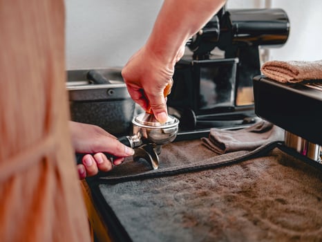 Barista presses ground coffee using a tamper in a coffee shop photo