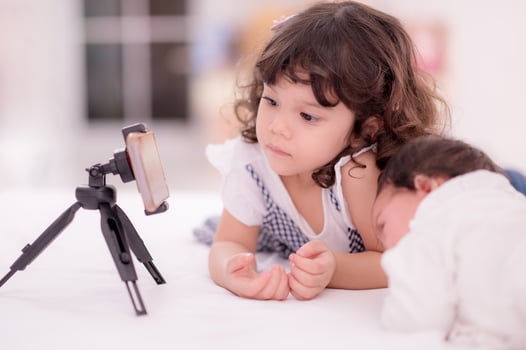 A cute Asian girl is looking at her mobile phone set to take a picture of herself and her newly born sister photo