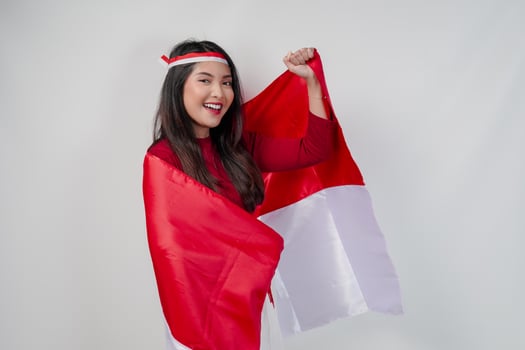 Happy young Asian woman with Indonesia flag draped over her shoulders and raising fist hand gesture. photo