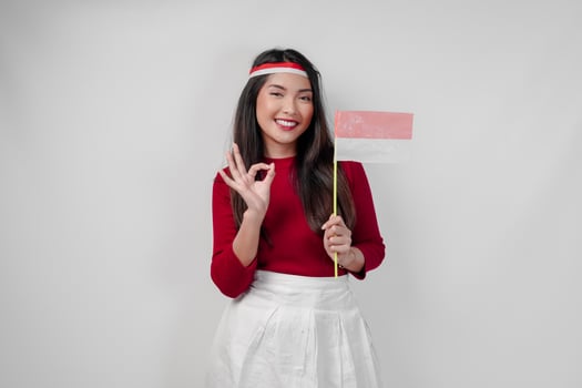 Beautiful young Asian woman is giving okay hand gesture while holding mini country flag. photo