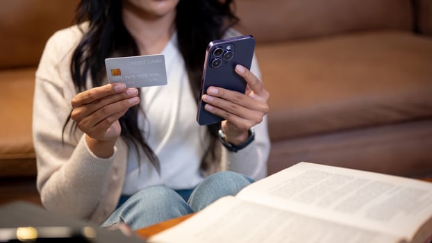 Cropped image of an Asian woman is holding a smartphone and a credit card, sitting in a living room. photo