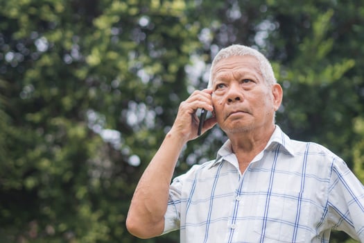 A senior man is using a smartphone looking up and a worried face while standing outdoors in the garden. Space for text. Aged people and communication concept photo