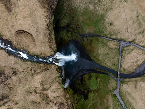 Aerial view of Seljalandsfoss waterfall in Iceland, cascading over cliffs into a serene pool surrounded by lush green landscape. photo