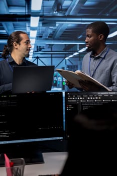 Manager getting feedback from engineer while overseeing data center, looking for firewall misconfigurations. Supervisor talking with workers in server room, asking about systems bottlenecks photo