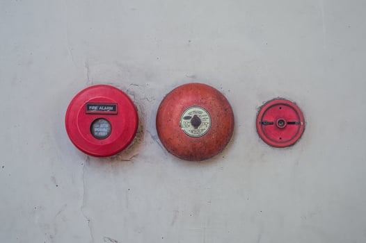 Retro fire alarm components attached to a white wall, such as a red break glass button and a bell. photo