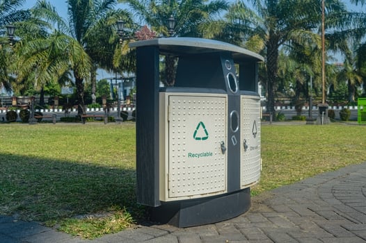 A modern, public recycling bin with a clear label and a green recycling symbol, placed in a park setting with palm trees in the background. photo