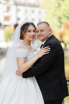 A bride and groom are posing for a picture. The bride is wearing a white dress and the groom is wearing a black suit. They are both smiling and seem happy photo