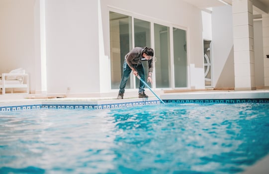 Person cleaning crystal clear pool with special brush. Home pool cleaning with wall brush photo
