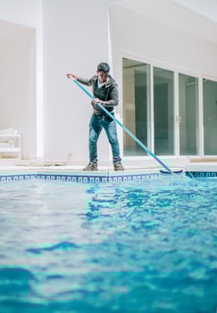 Home pool cleaning with wall brush. Male worker cleaning a home swimming pool with special brush photo