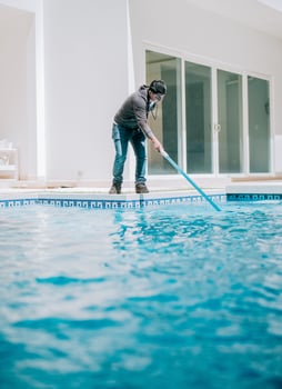 Young man cleaning a swimming pool with suction hose. Swimming pool cleaning and maintenance service photo