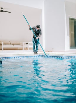 Male worker cleaning a home swimming pool with special brush. Home pool cleaning with wall brush photo