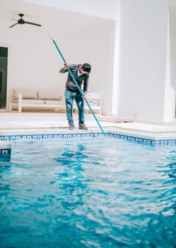 Worker cleaning a beautiful homemade swimming pool with skimmer. Maintenance person cleaning a beautiful home swimming pool photo