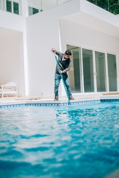 Maintenance person cleaning a beautiful home swimming pool. Worker cleaning a beautiful homemade swimming pool with skimmer photo